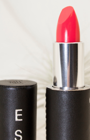 Close-up of La Bouche Rouge lipstick packaging showing the dark vegan leather case, magnetic lid, and striking Peach Balm lipstick shade. The case features personalized letter engraving options.