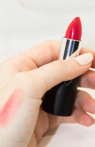 Close-up of La Bouche Rouge lipstick packaging showing the dark vegan leather case, magnetic lid, and striking Peach Balm lipstick shade. The case features personalized letter engraving options.