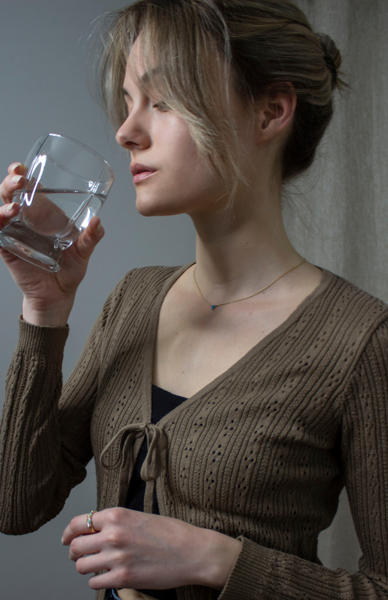 An image of a woman drinking a glass of water, demonstrating one of the essential healthy habits for maintaining a glowing, healthy skin.