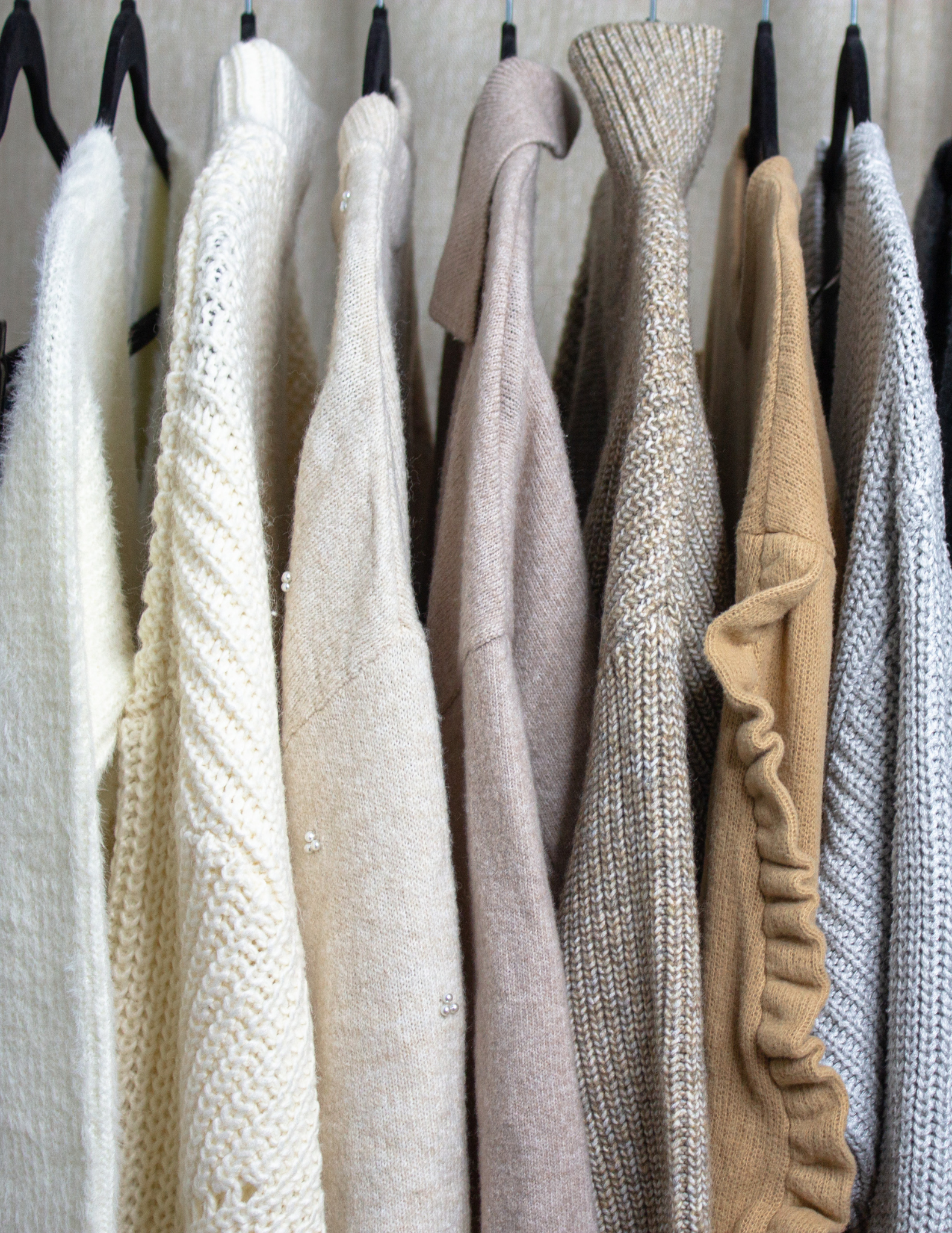 In the image, a clothing rack displays an array of luxurious cashmere and sophisticated fine-knit sweaters. The collection includes various colors such as white, cream, beige, light brown, mustard, and light blue, embodying quiet luxury, timeless elegance, and classic, neutral color palette.