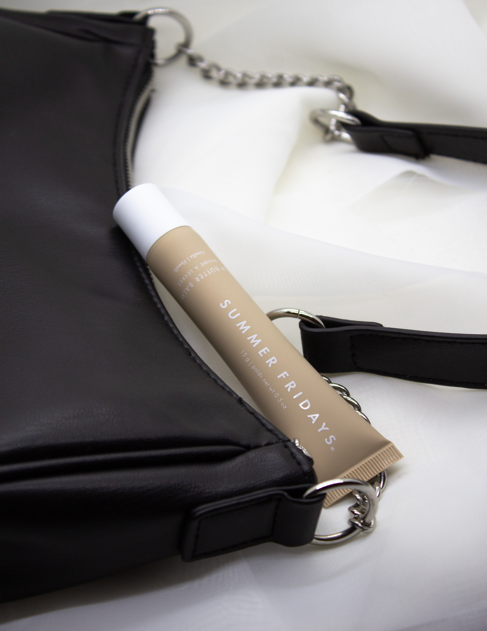 Summer Fridays Lip Butter Balm displayed alongside a stylish black purse, highlighting the sleek packaging against the dark backdrop.