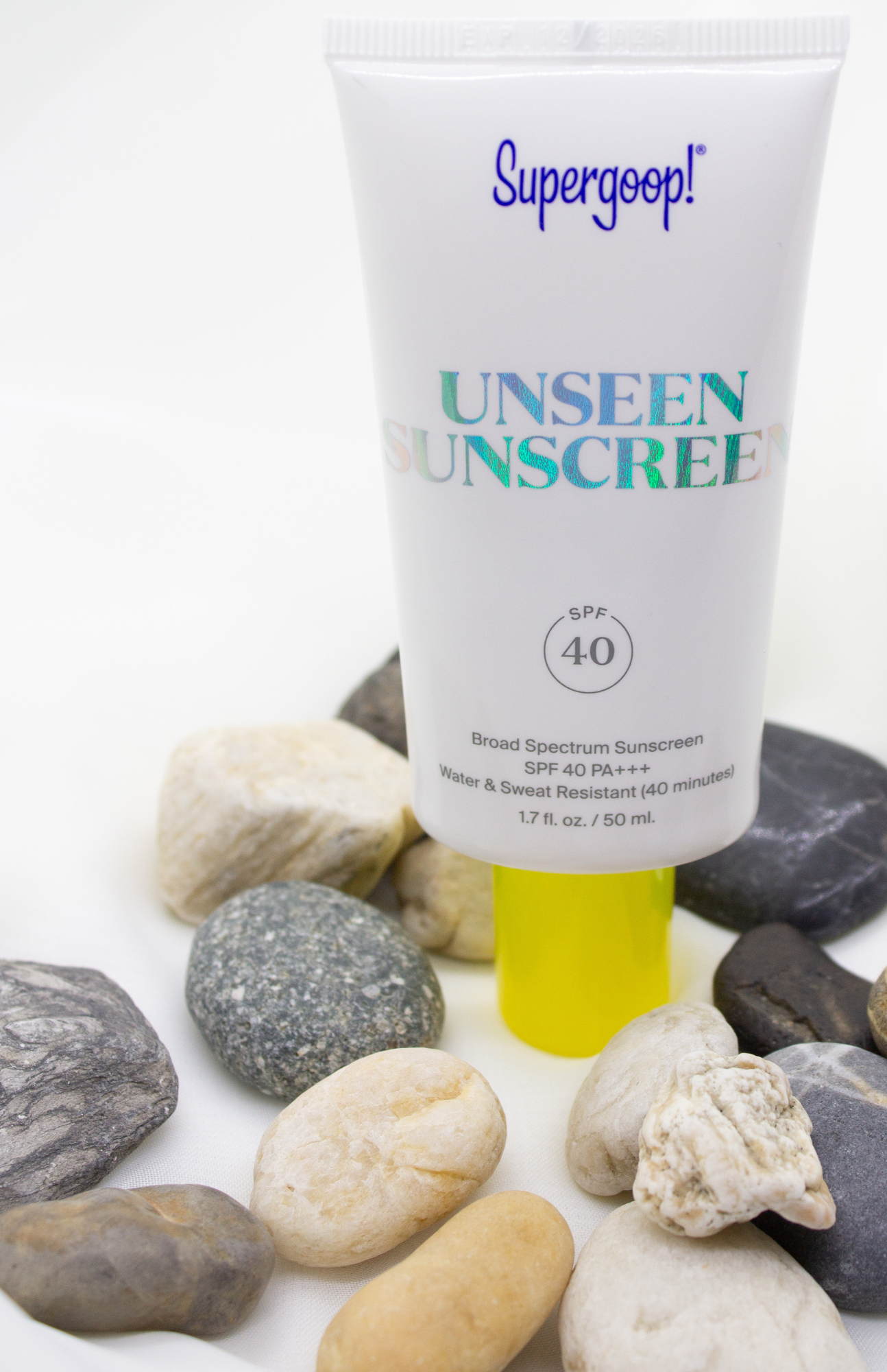 The image captures the elegance of Supergoop! Unseen Sunscreen SPF 40 PA+++, beautifully displayed against a soft, neutral backdrop with small beach pebbles.