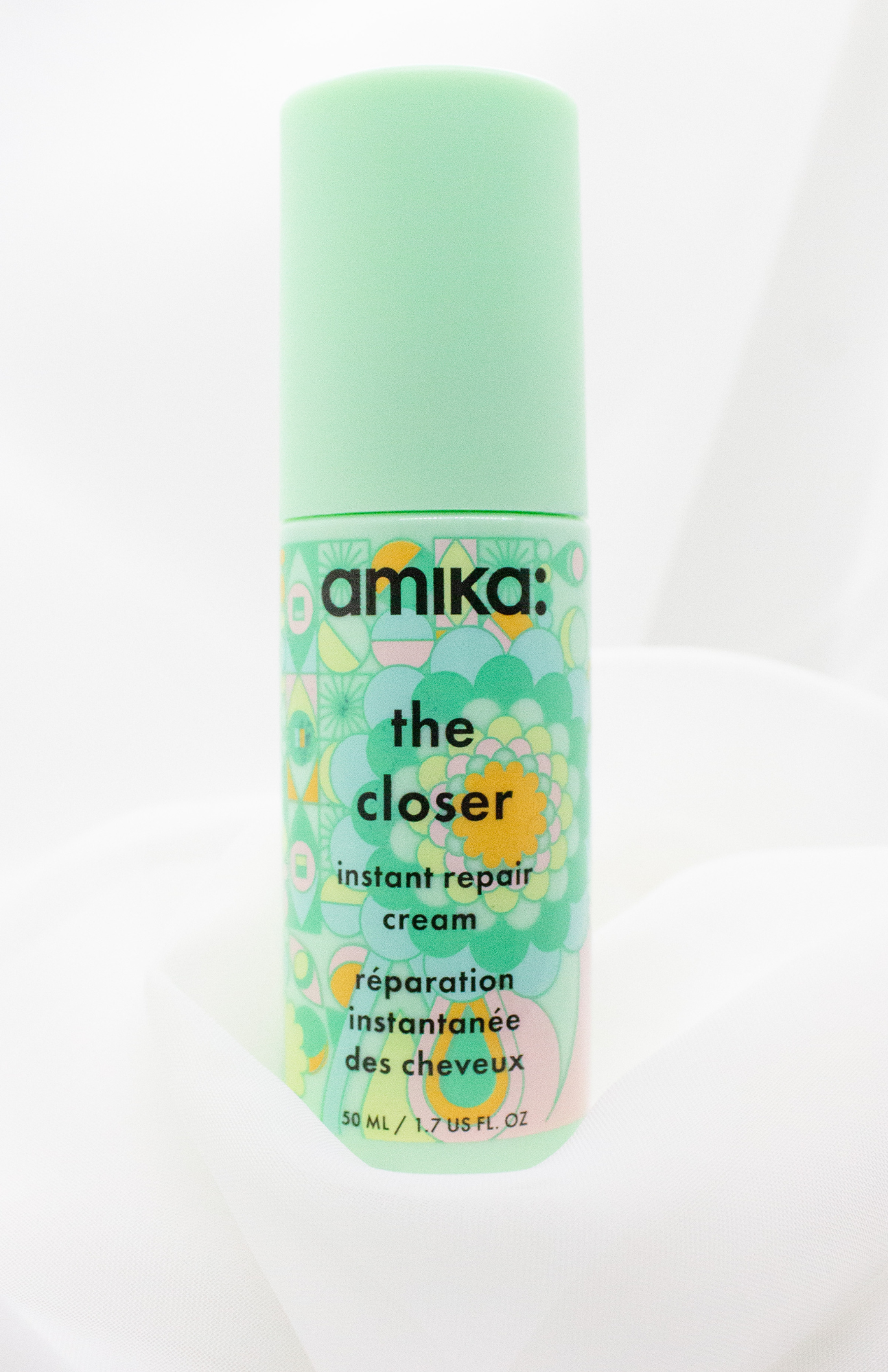 Amika The Closer Instant Repair Cream bottle elegantly displayed against a soft off white background, highlighting its sleek design and vibrant packaging.