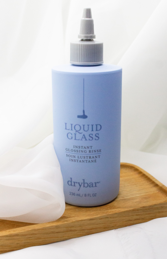 A bottle of Drybar Liquid Glass Instant Glossing Rinse elegantly showcased against a soft, white, veil-like background.