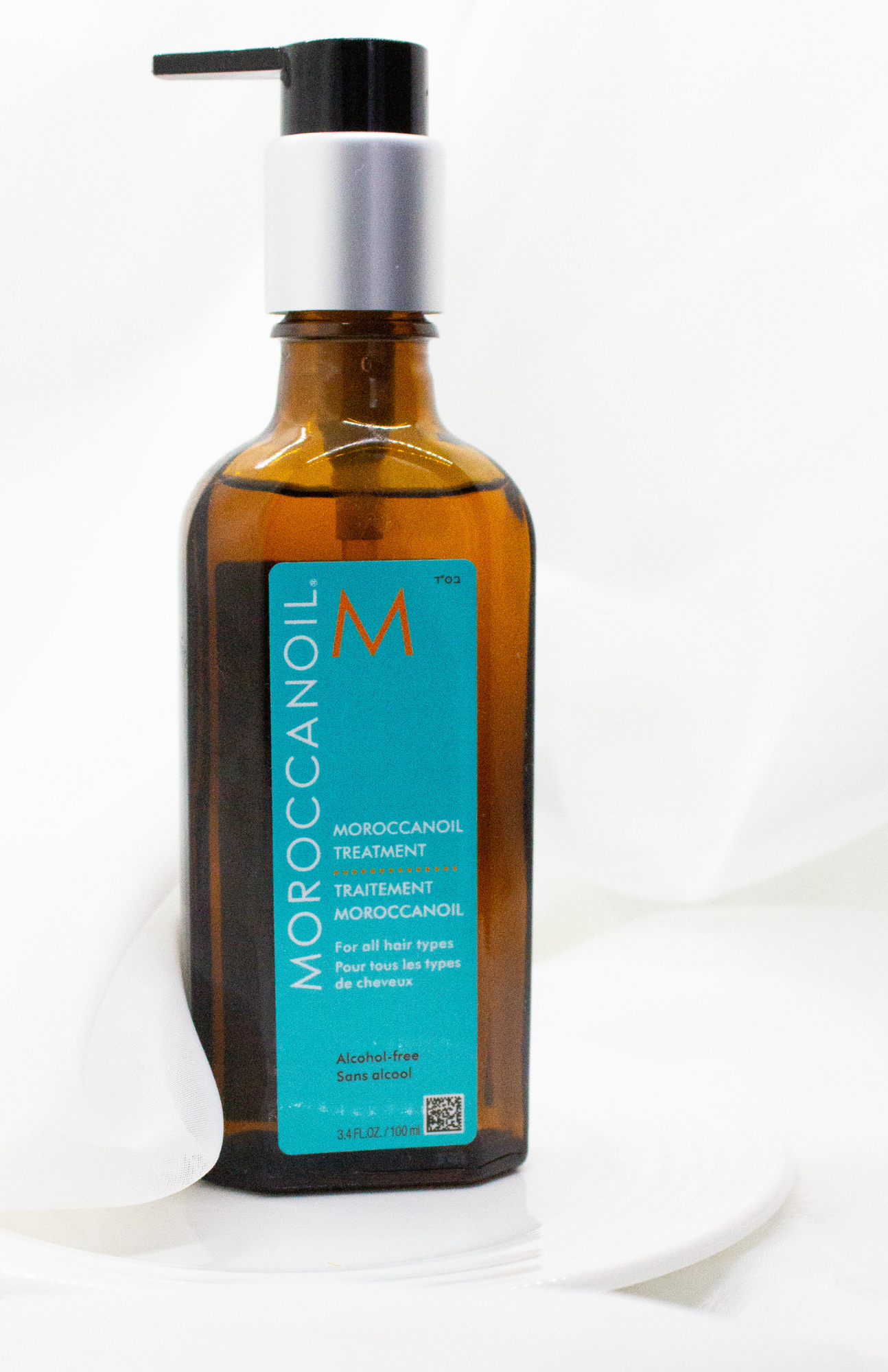 Moroccanoil Hair Treatment packaging featuring a vibrant blue label on an amber glass bottle with a pump, elegantly displayed against a soft white background to highlight its sleek design and eye-catching colors.