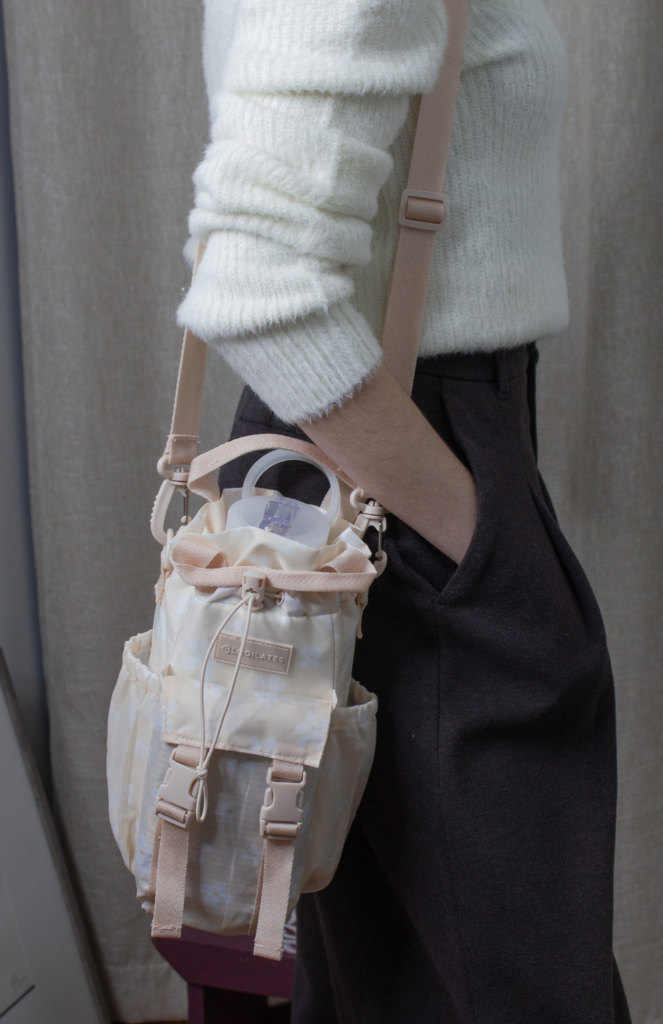 Content creator modeling the Blogilates water bottle bag, styled with an ivory H&M Divided V-neck sweater and dark brown UNIQLO pleated wide pants, showcasing its versatility with a stylish work-ready outfit.