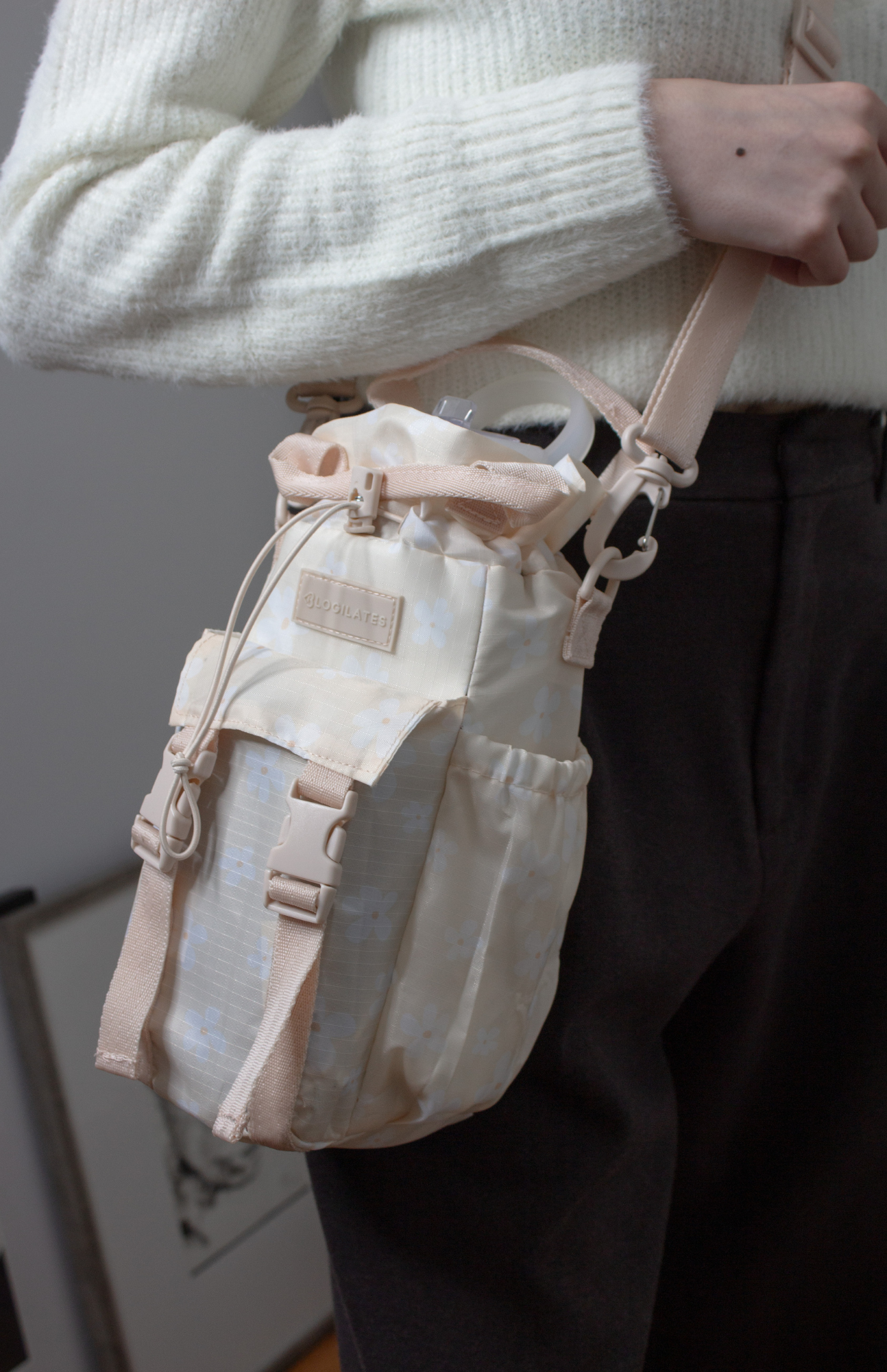 Content creator modeling the Blogilates water bottle bag, styled with an ivory H&M Divided V-neck sweater and dark brown UNIQLO pleated wide pants, showcasing its versatility with a stylish work-ready outfit.