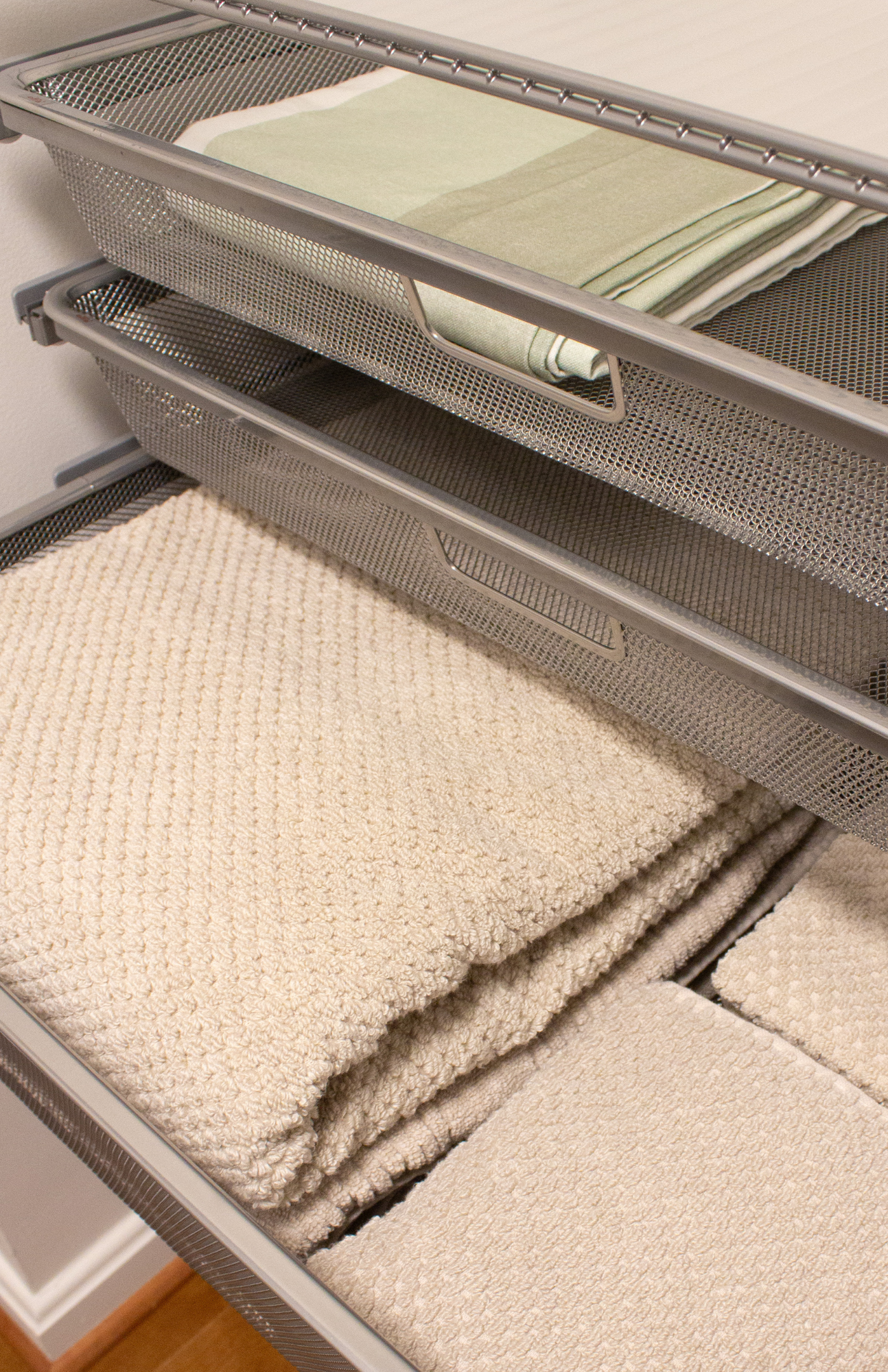 Beautifully organized closet drawers neatly storing bath towels and clothing in calming beige and green tones, creating a functional, clutter-free space that helps maximize your closet space.