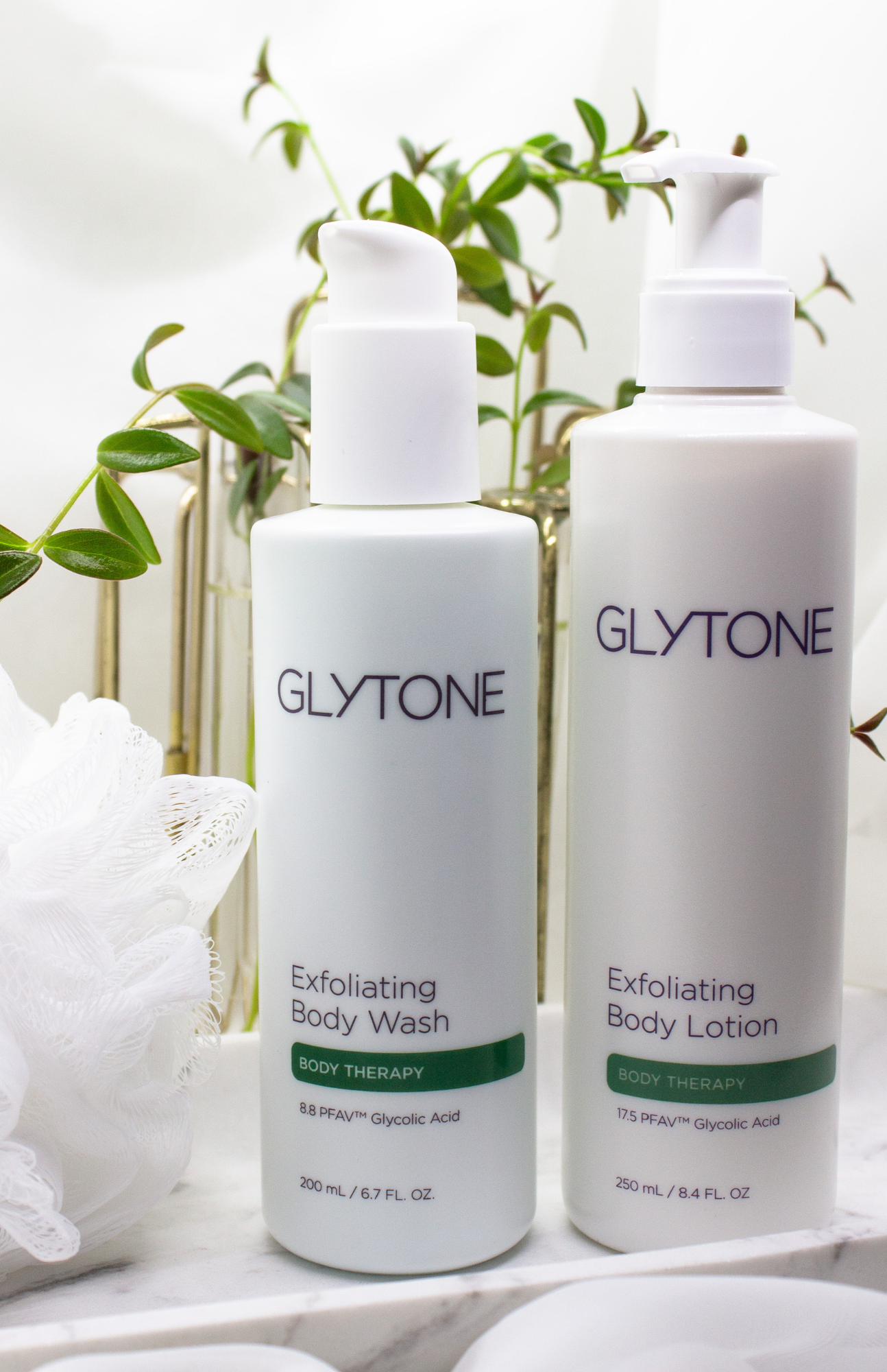 Glytone Exfoliating Body Wash and Body Lotion displayed on a white background with greenery, ideal for smoothing rough, bumpy skin.