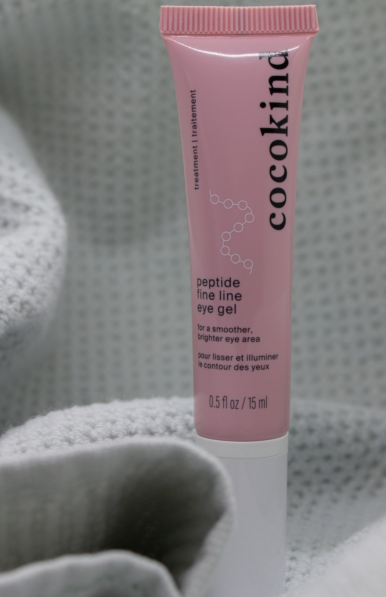 Cocokind Peptide Eye Gel standing upright against a soft textured light green towel background, showcasing clean skincare with peptides and ceramides.