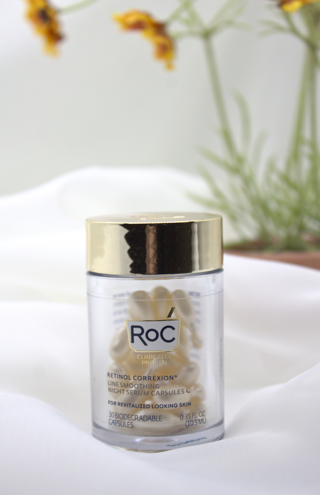 RoC Clinically Proven Retinol Correxion Line Smoothing Night Serum Capsules jar on soft white background with a delicate yellow flower, showcasing the skincare product for sensitive skin.