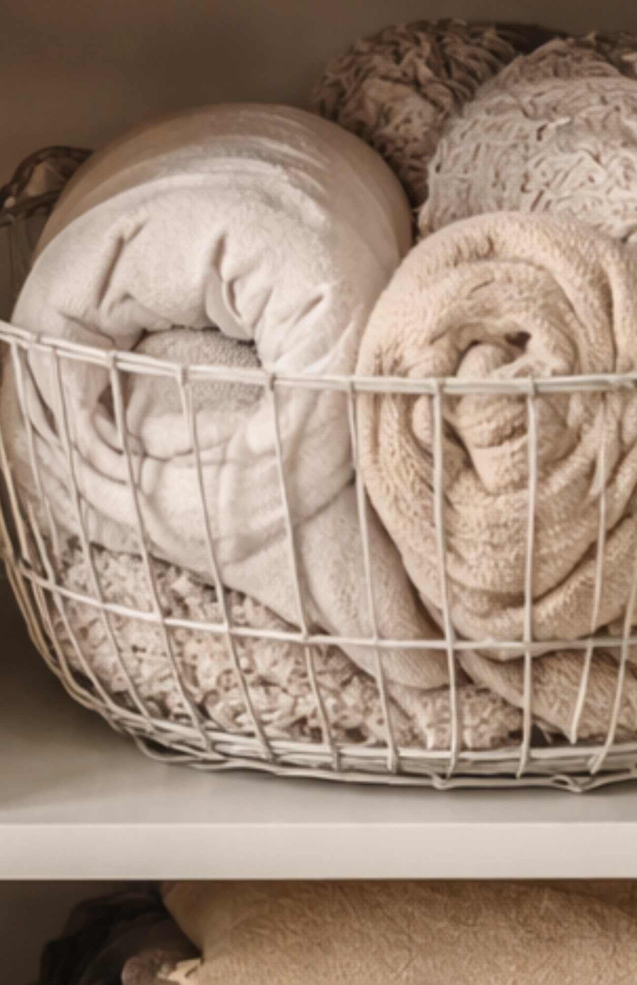 Blankets and throws neatly organized in a wire basket for a clutter-free linen closet.