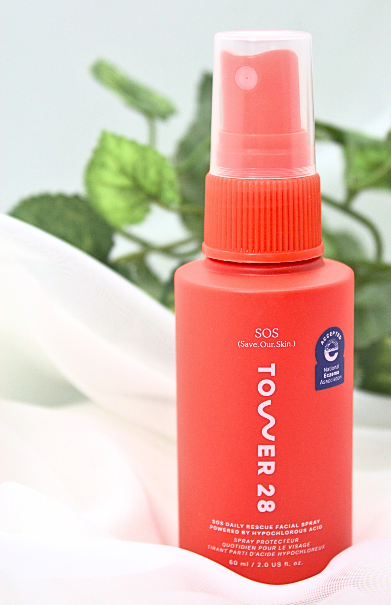 Tower 28 Hypochlorous Acid SOS Rescue Spray bottle displayed on a soft white background with green foliage, highlighting the calming facial mist for sensitive skin.