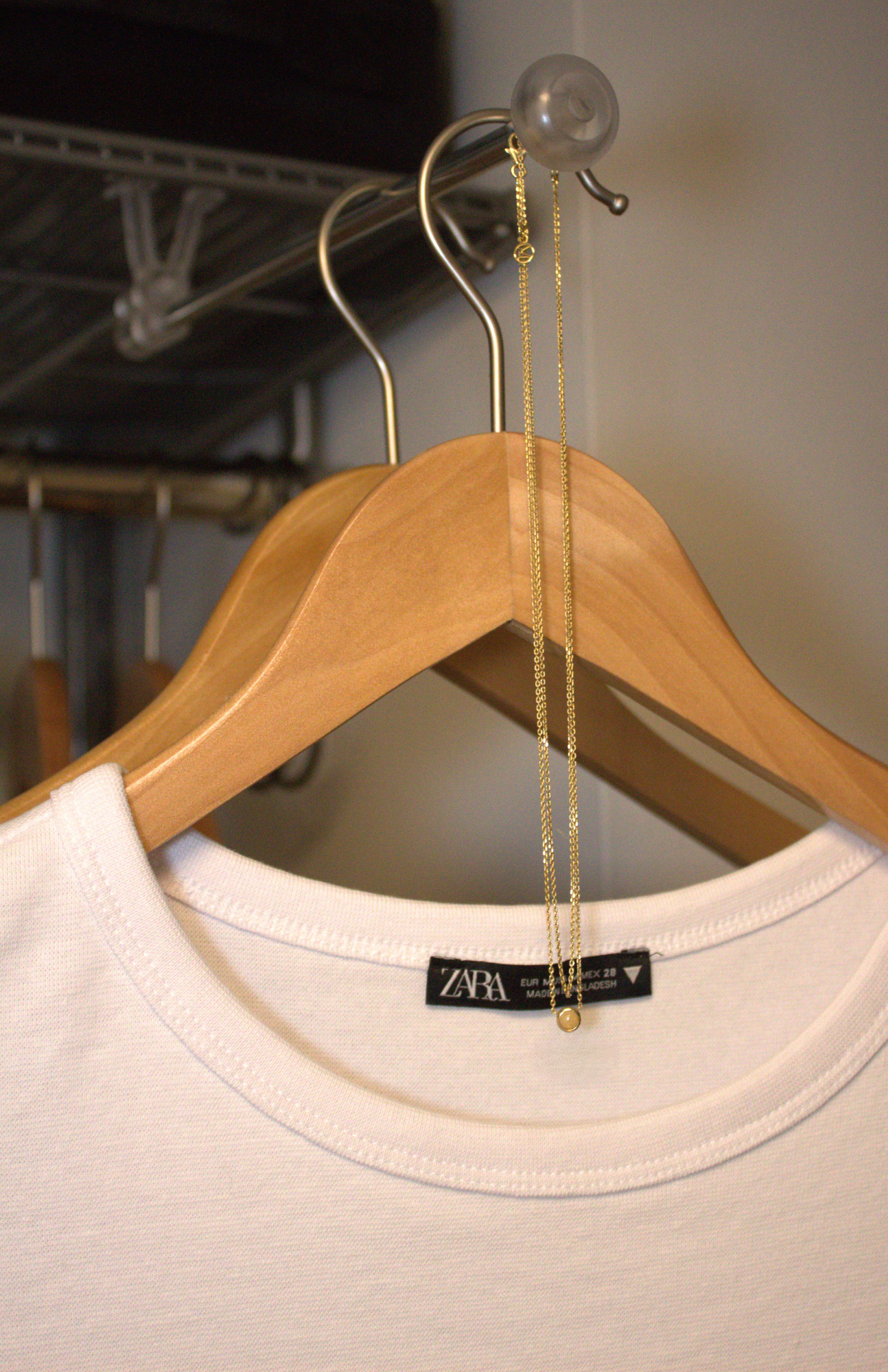 Minimalist white shirt hanging on a wooden hanger in an organized closet with a delicate gold necklace.